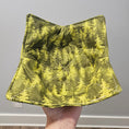 Load image into Gallery viewer, Tree camouflage-patterned bowl cozy held by a hand against a neutral background
