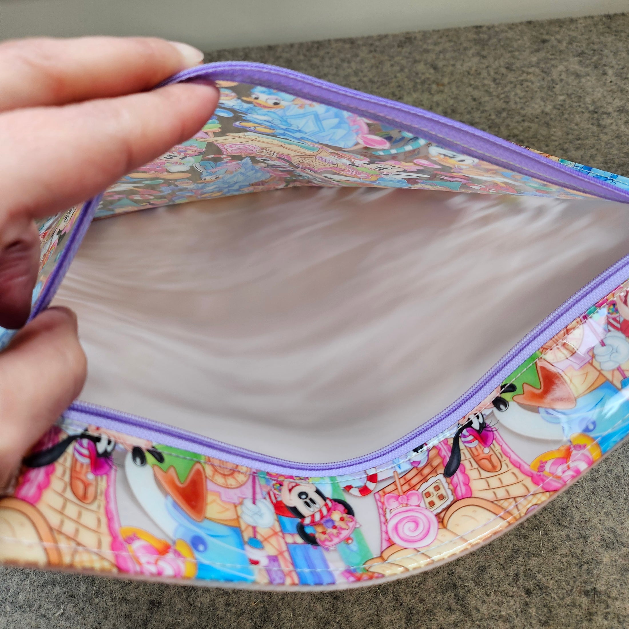 Colorful fabric pouch with cartoon designs held by a hand on a neutral background