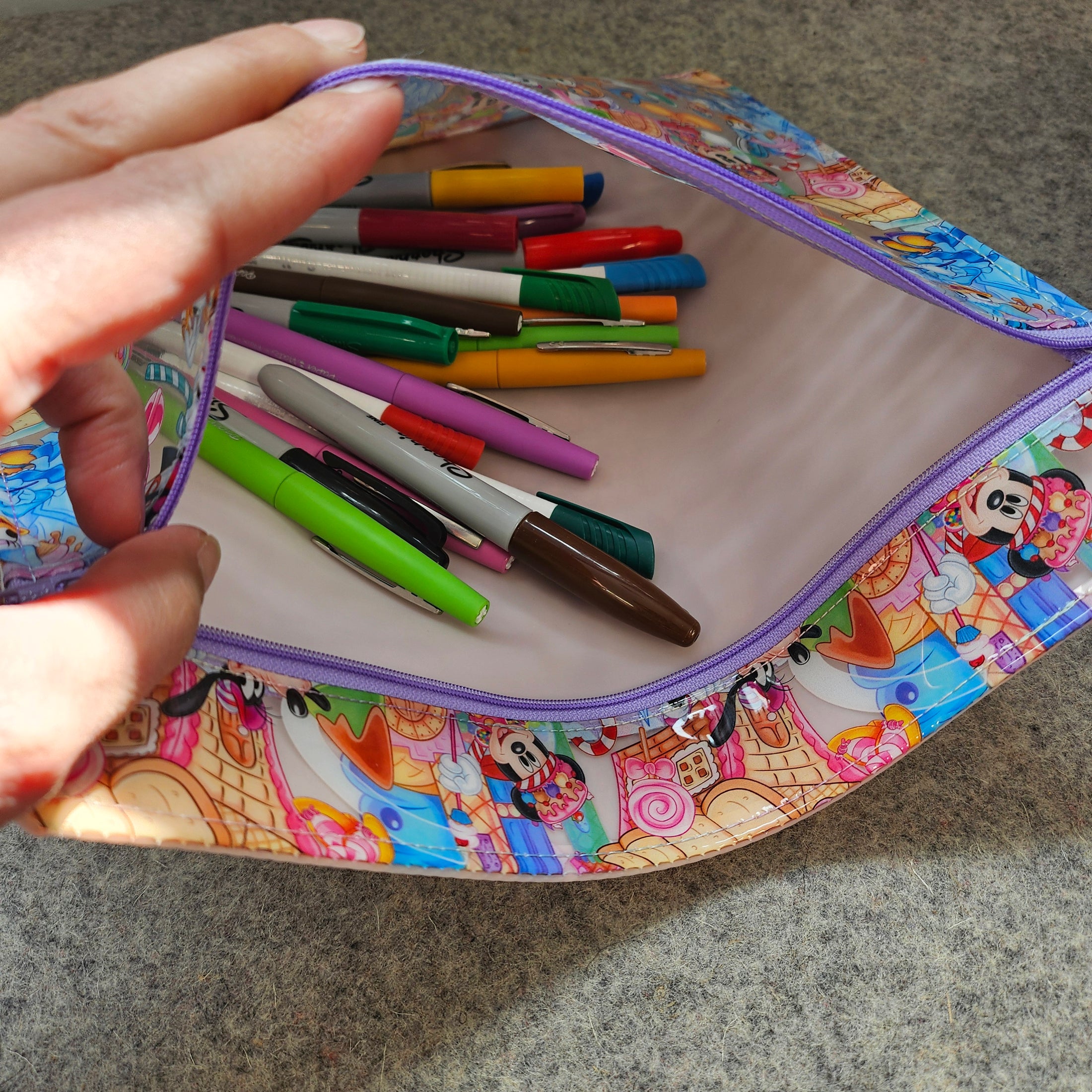 Colorful pencil case with cartoon design containing pens on a gray surface