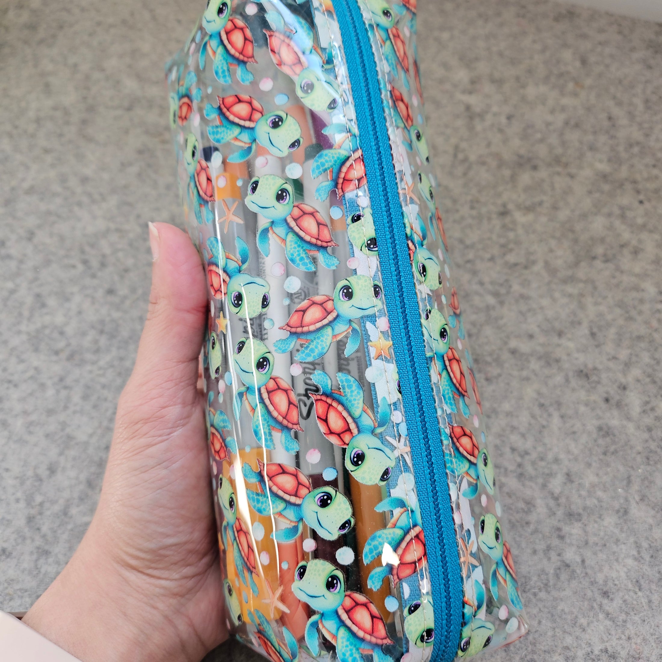 Pencil case with turtle pattern held by a hand on a neutral background