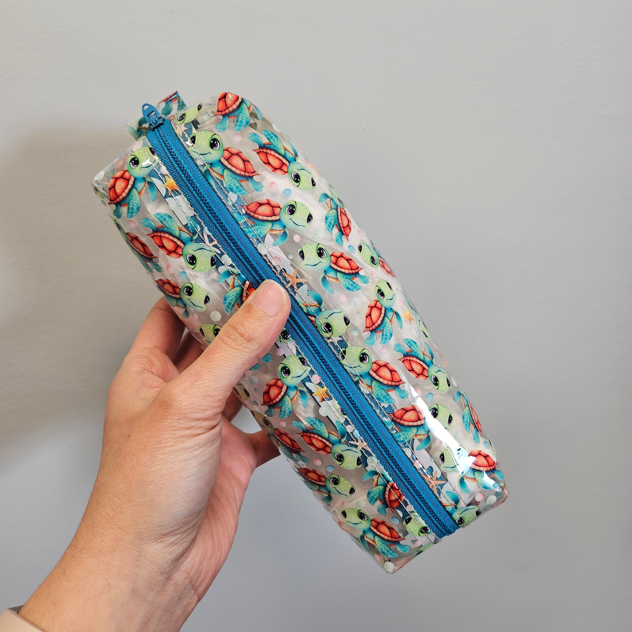 Hand holding a cylindrical pouch with a colorful pattern against a gray background