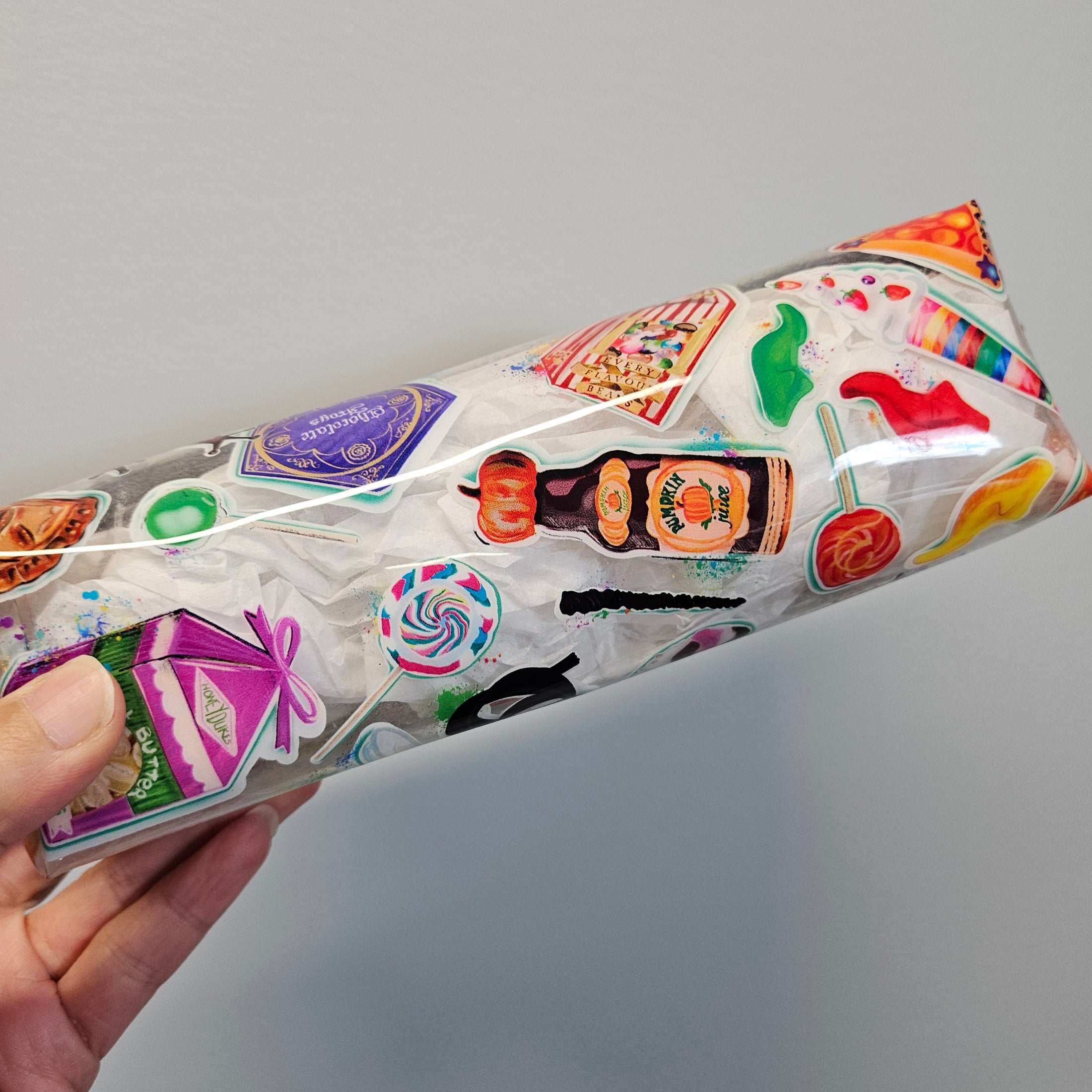 Hand holding a transparent bag with colorful stickers against a gray background