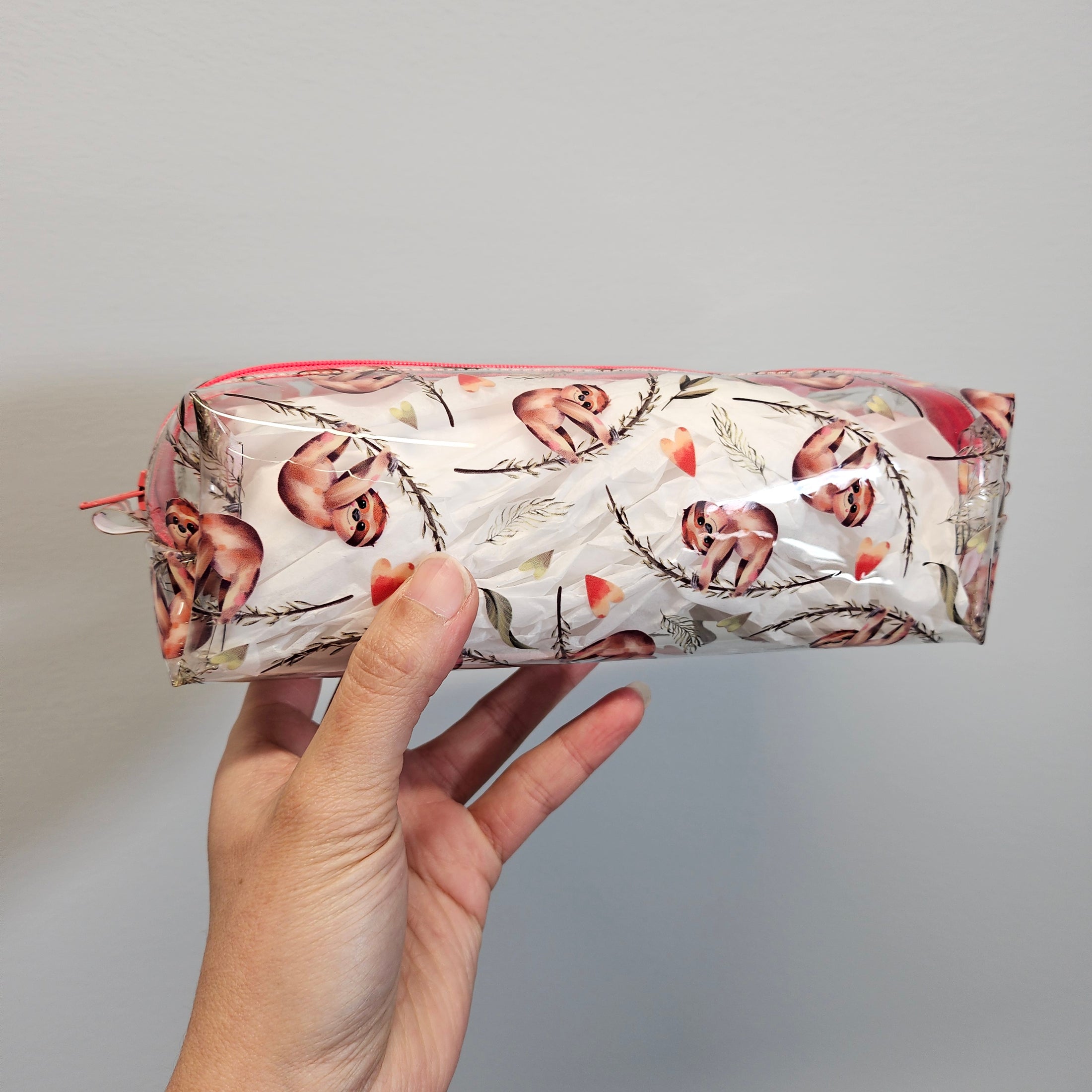 Hand holding a transparent package with printed design against a gray background