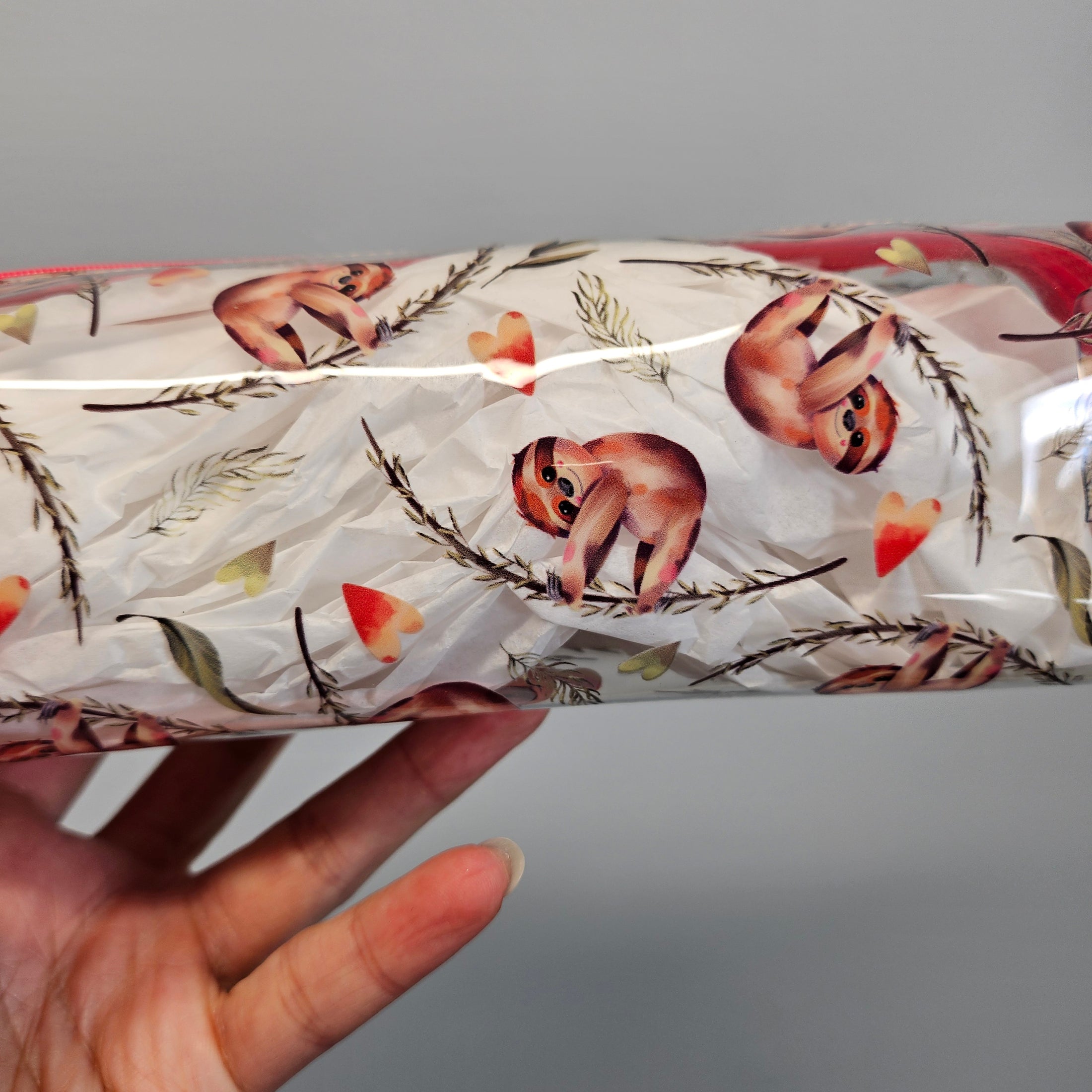 Tumbler with sloth design held by a hand against a gray background