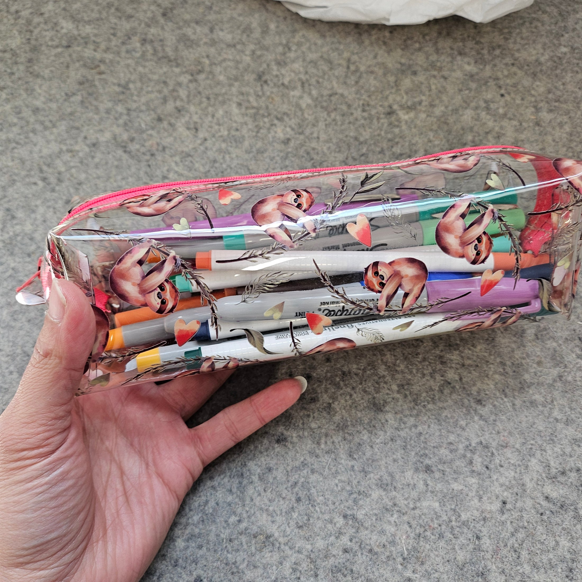 Pencil case with sloth design held by a hand on a gray surface