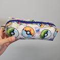 Load image into Gallery viewer, Pouch with Poké Ball designs held by a hand against a gray background
