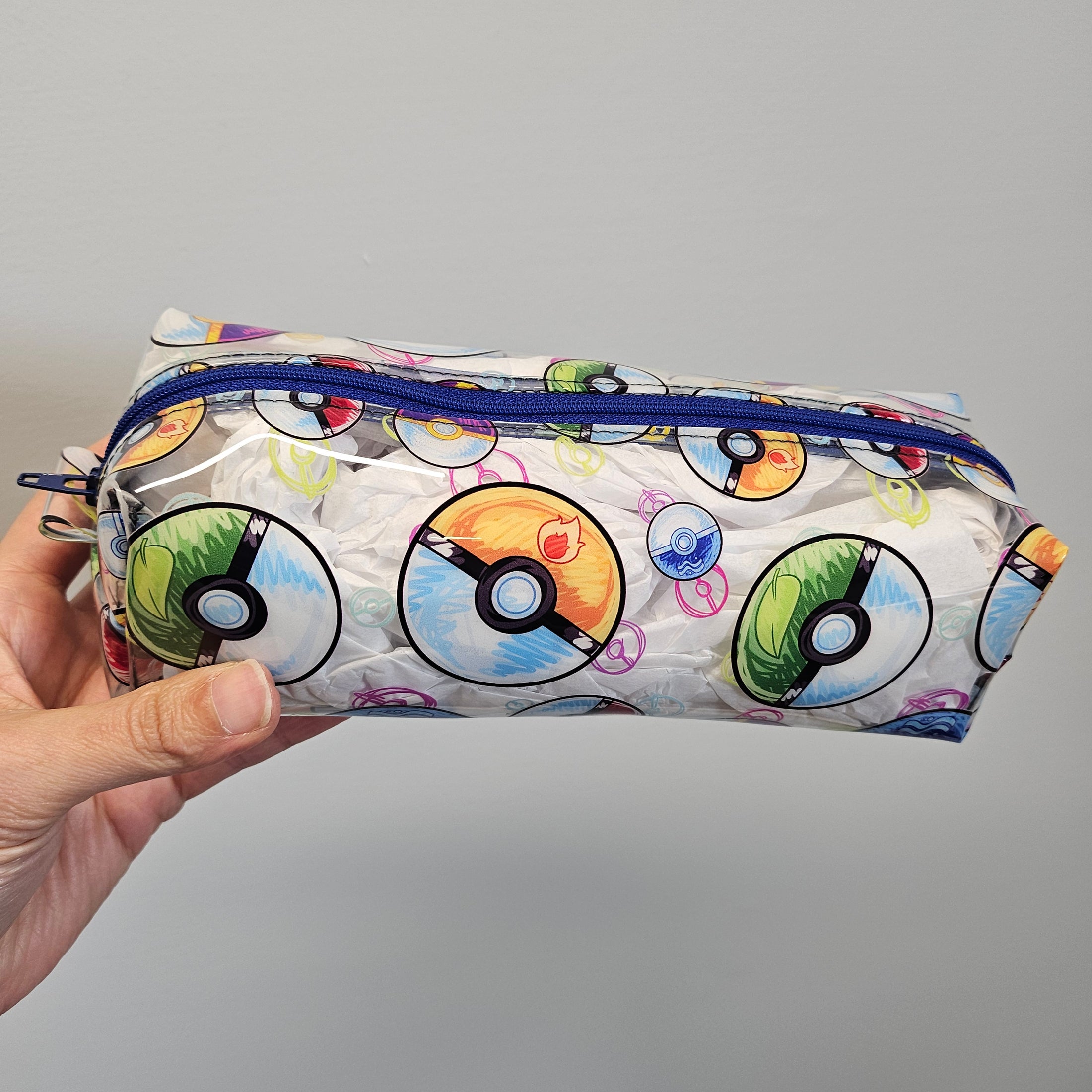 Pouch with Poké Ball designs held by a hand against a gray background