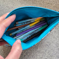 Load image into Gallery viewer, Blue pencil case with markers held by a hand on a concrete surface
