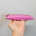 Load image into Gallery viewer, Hand holding a pink pouch with a zipper against a gray background
