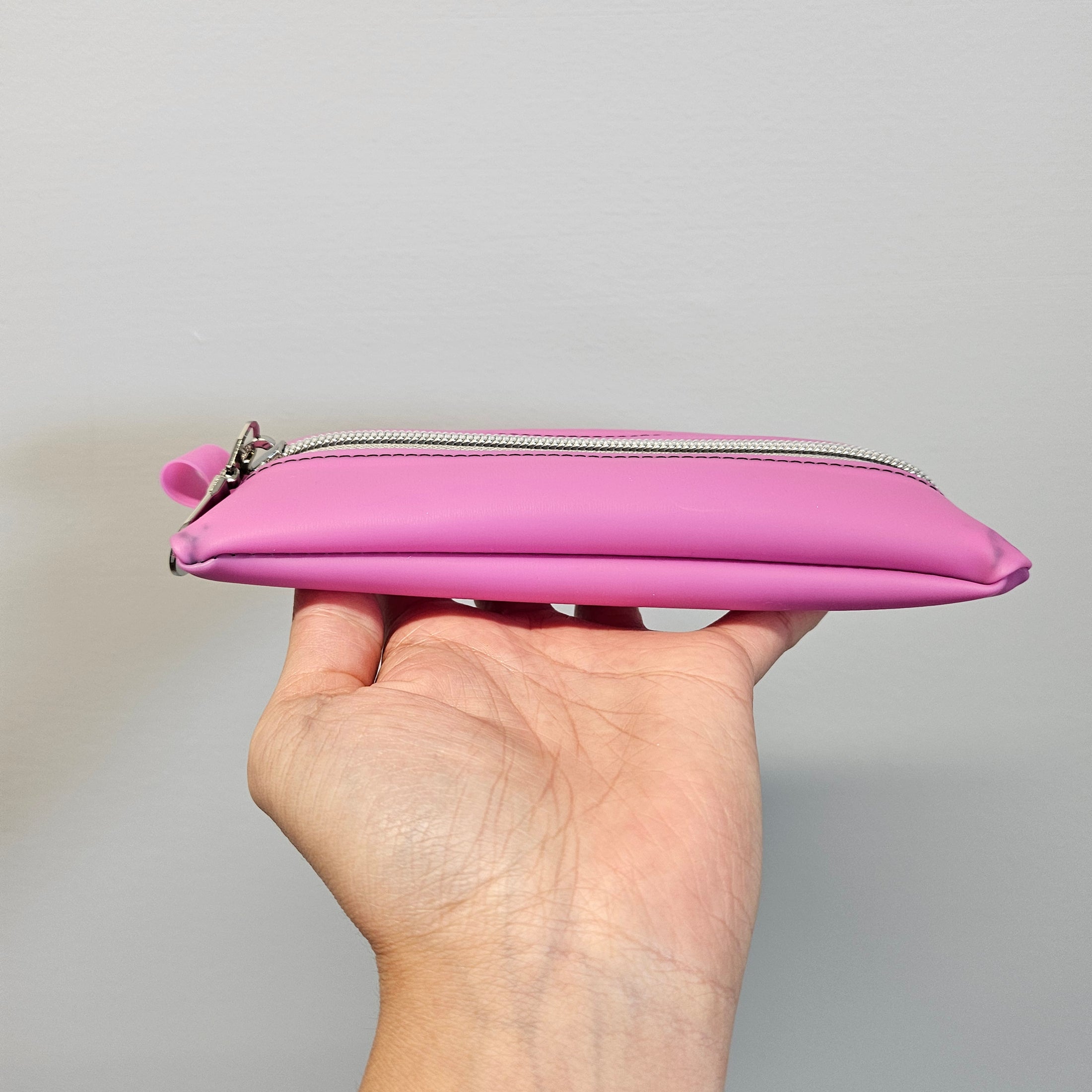 Hand holding a pink pouch with a zipper against a gray background