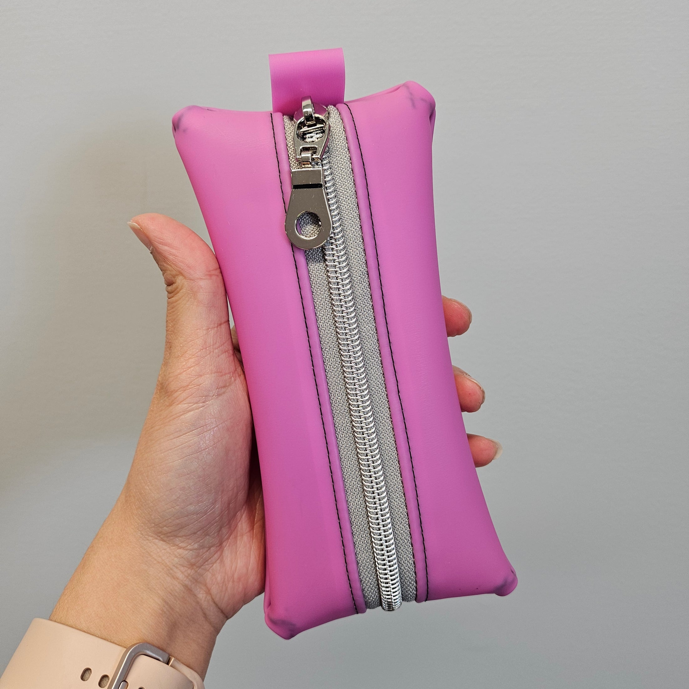 Hand holding a pink pouch with a silver zipper against a gray background