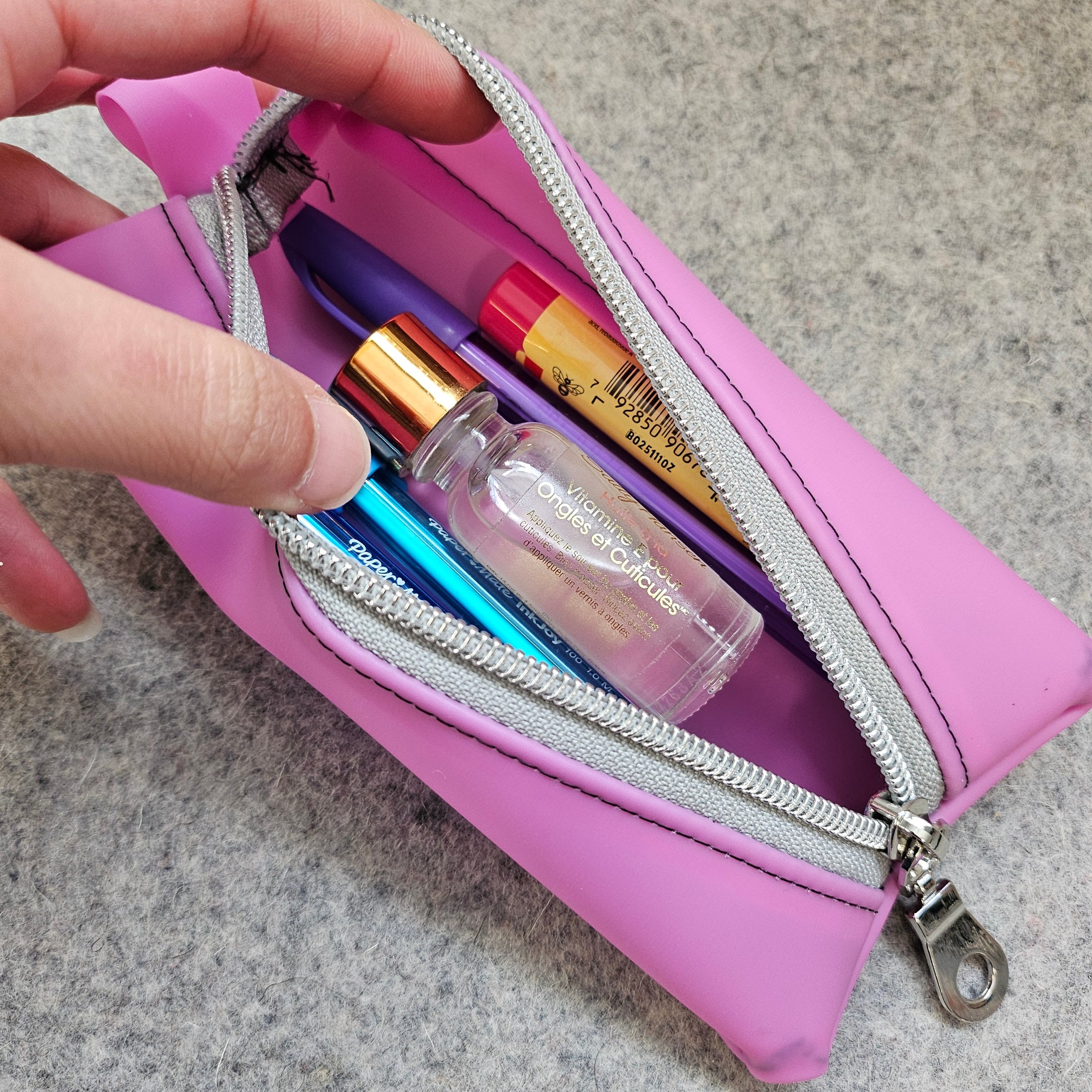 Pink makeup pouch with lipsticks and a nail file on a gray surface