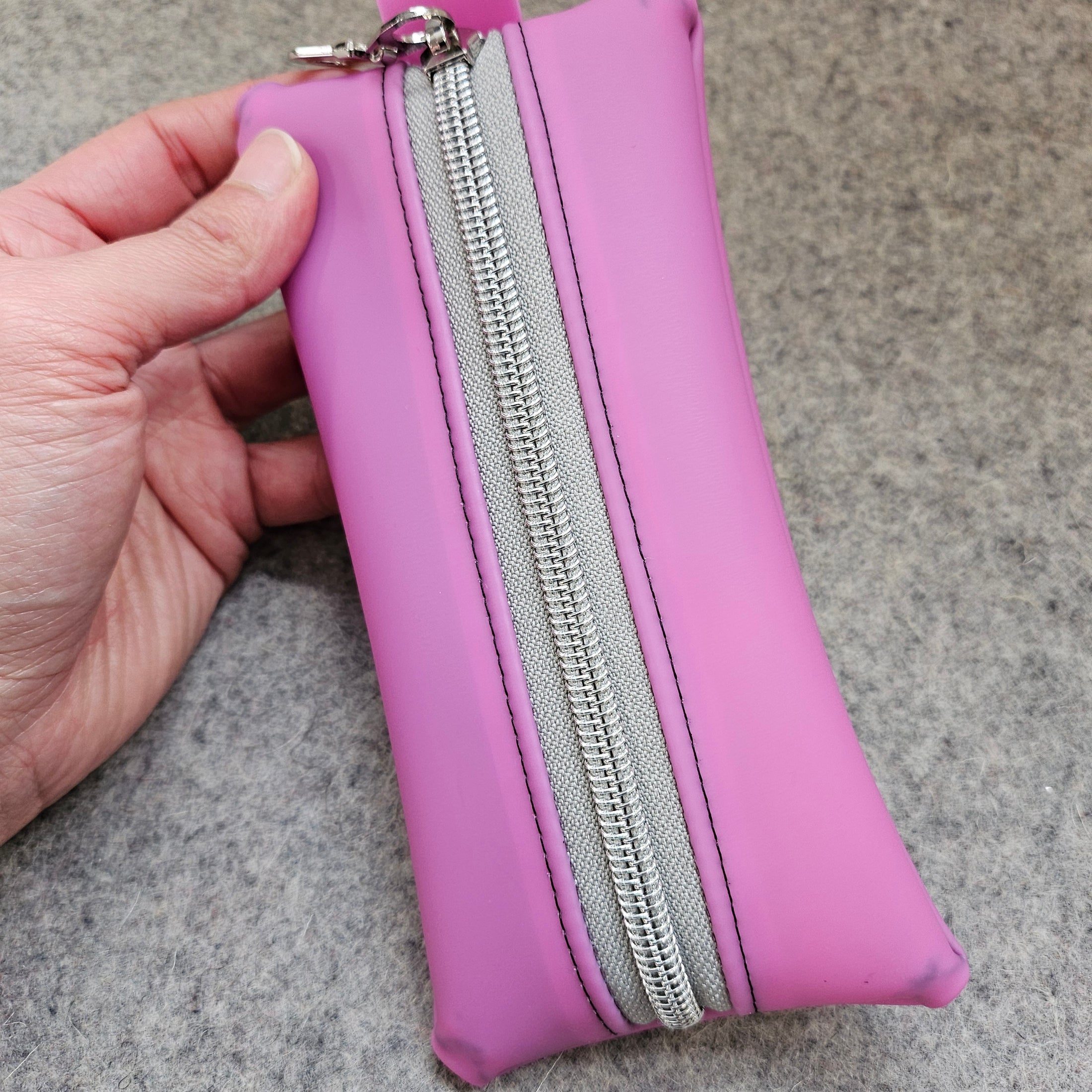 Purple pouch with a silver zipper held by a hand on a gray background