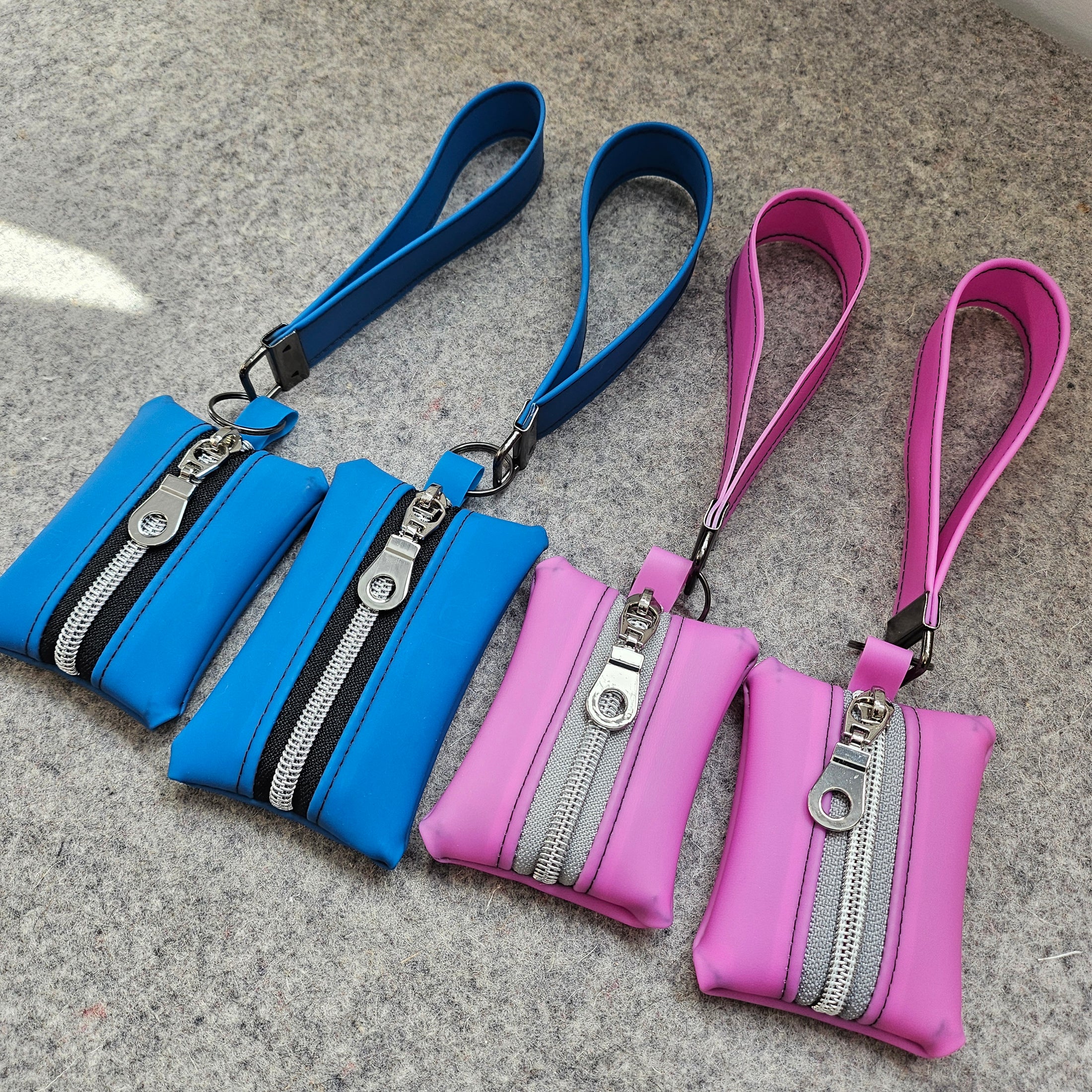 Two pink and two blue zipper pouches with wrist straps on a gray surface