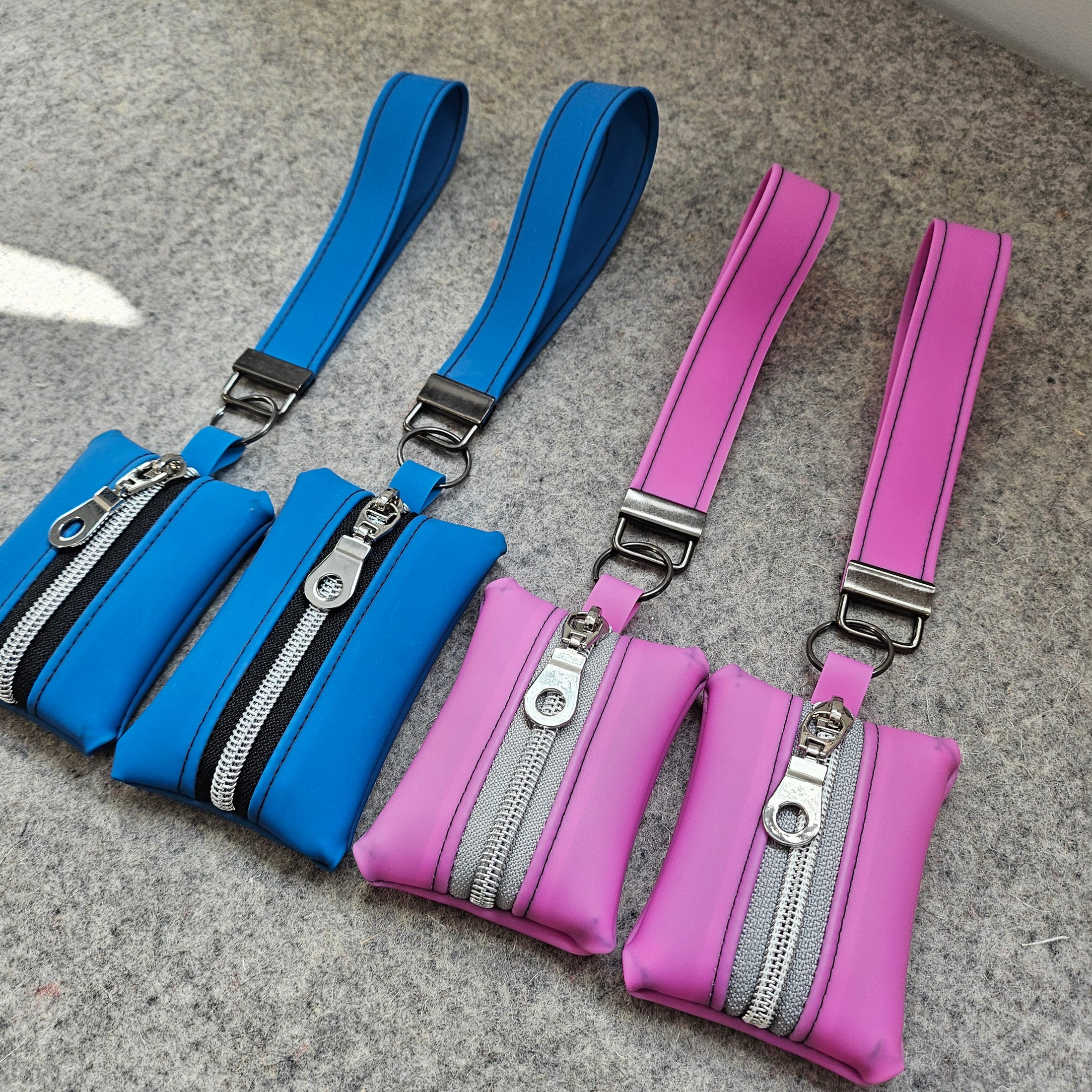 Two waist bags, one pink and one blue, with zippers on a gray surface.
