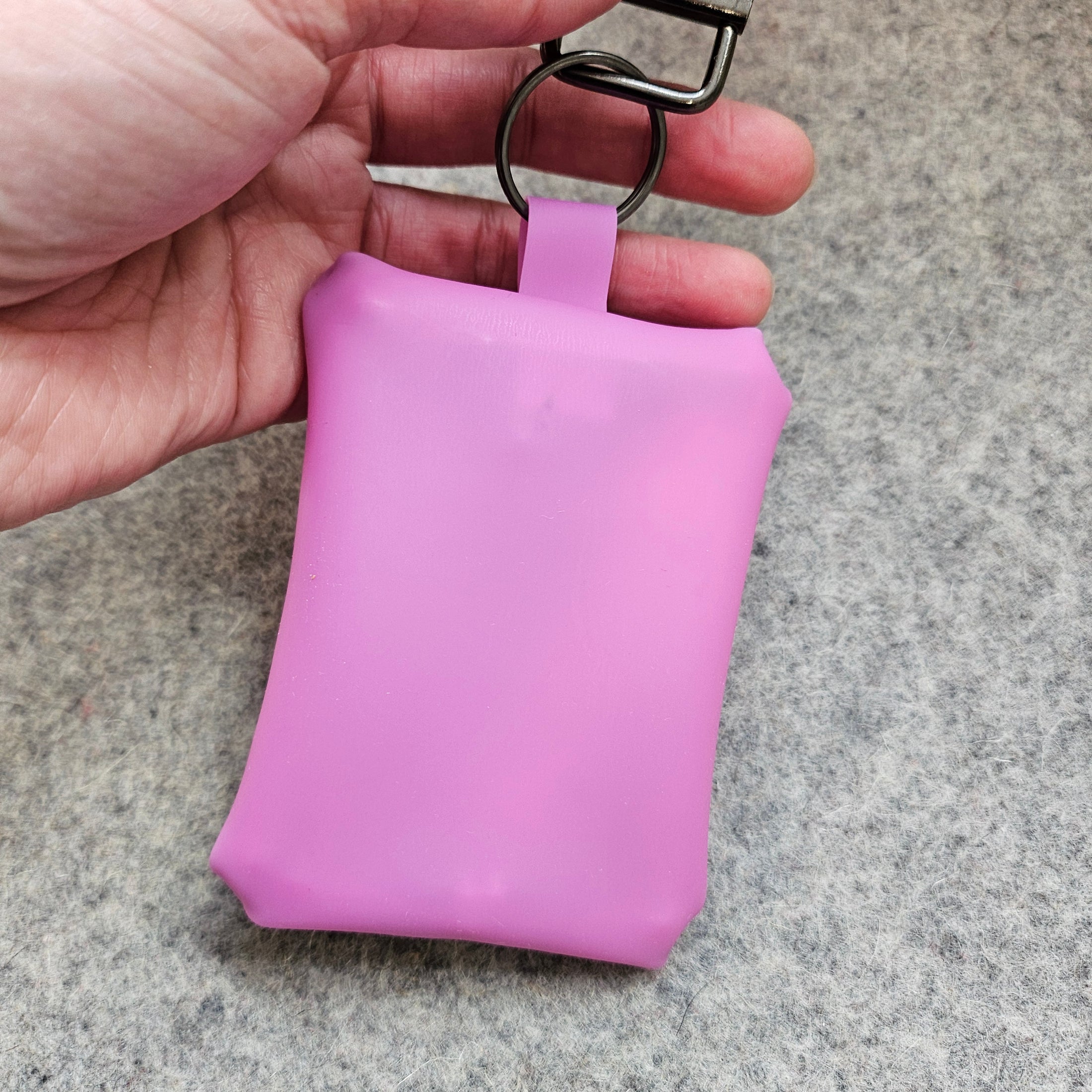 Hand holding a small pink pouch with a keychain on a gray surface