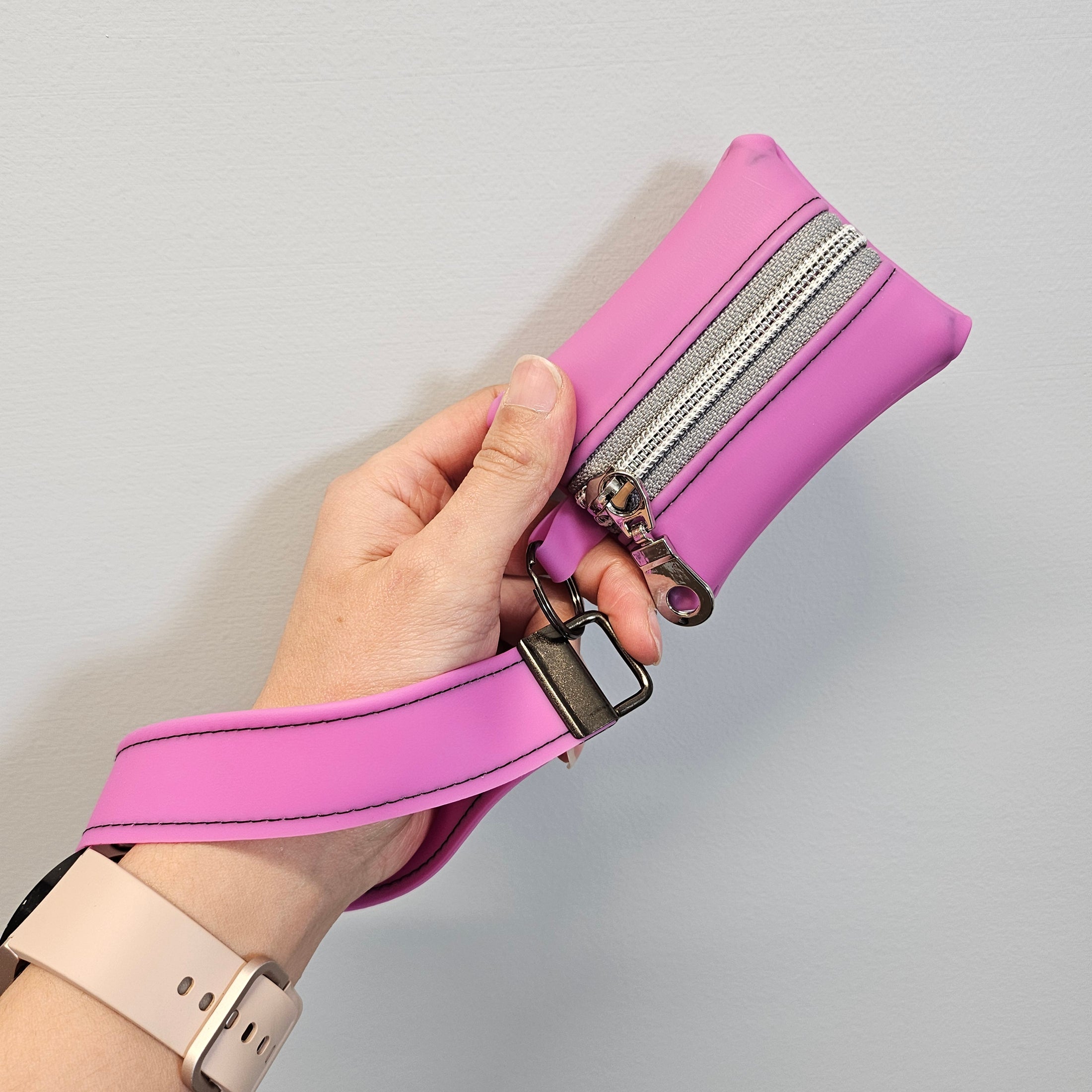 Pink leather bag with a strap held by a hand on a light gray background