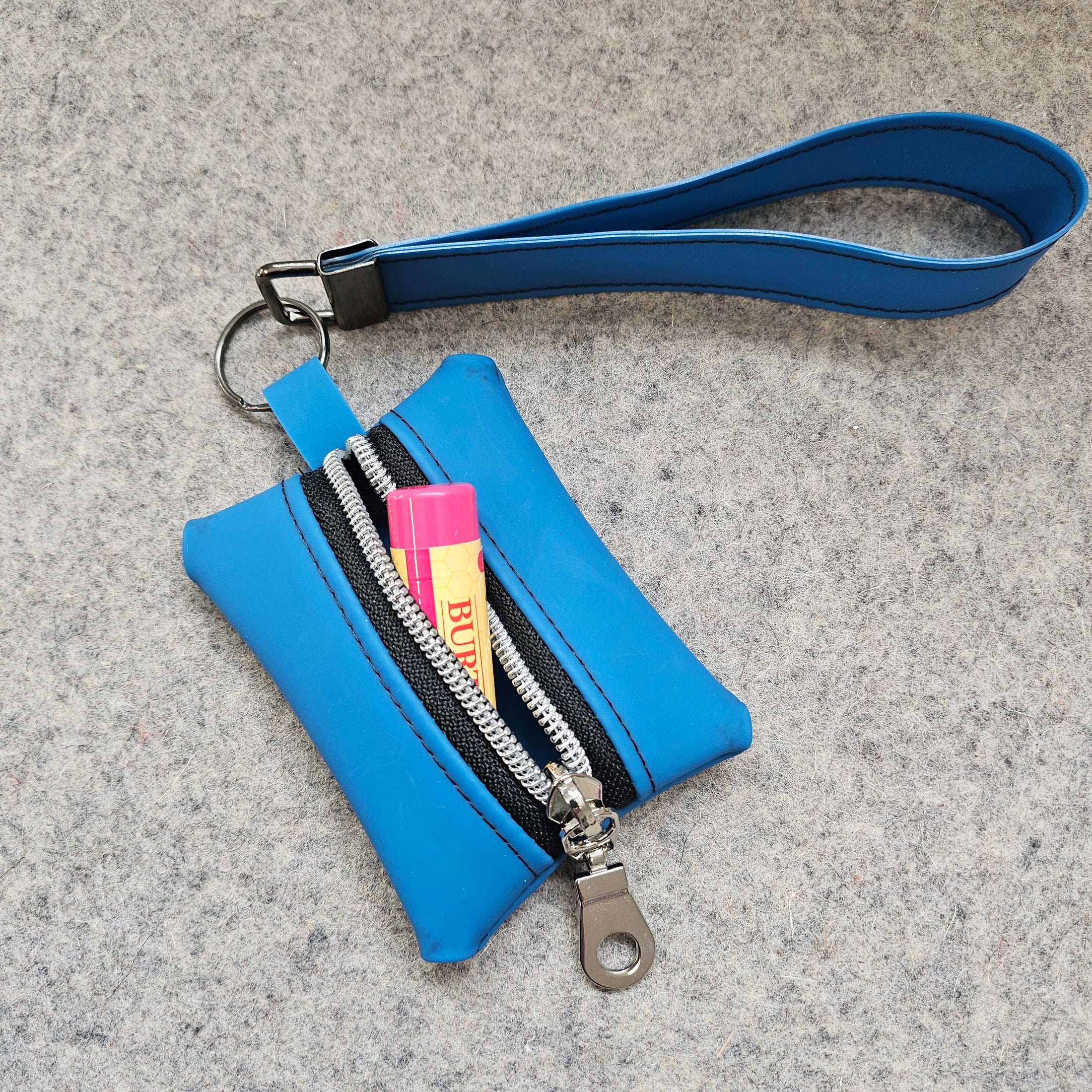 Blue keychain pouch with wrist strap and Burts Bees lip balm on a gray surface