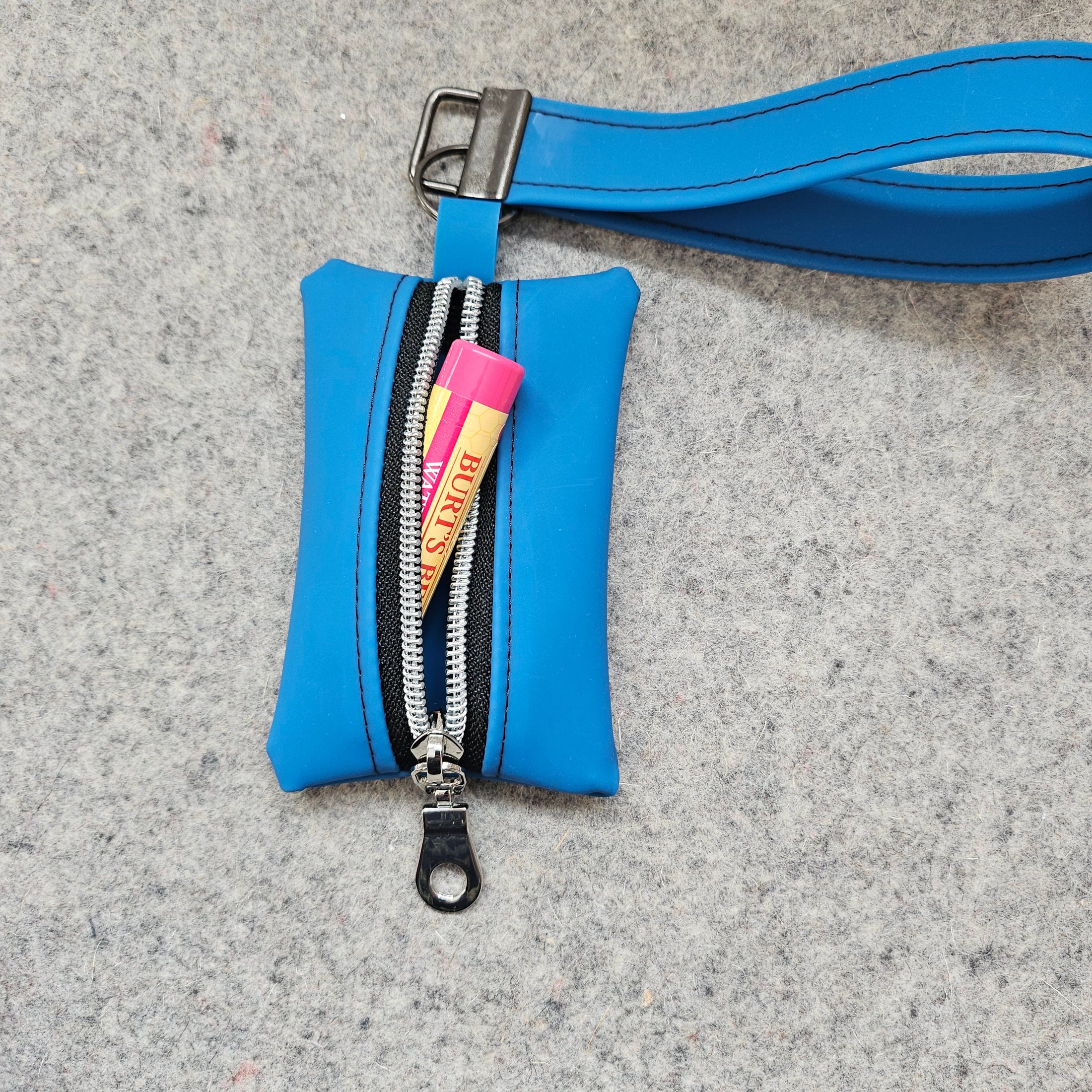 Blue pouch with a strap and Burt's Bees product on a gray surface