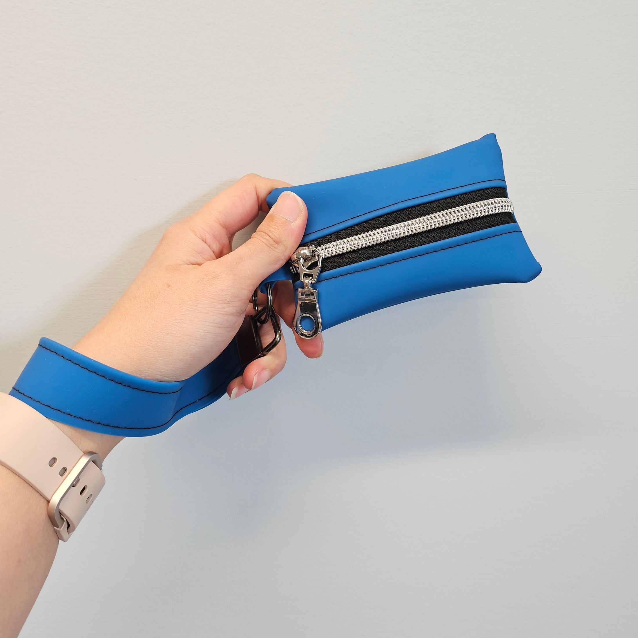 Hand holding a blue wallet with a zipper against a light gray background