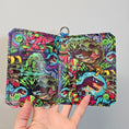 Load image into Gallery viewer, Colorful patterned pouch held by a hand on a gray background
