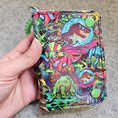 Load image into Gallery viewer, Colorful dinosaur-patterned pouch held by a hand on a gray surface
