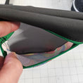 Load image into Gallery viewer, Close-up of a hand holding a black and green bag with a colorful interior.

