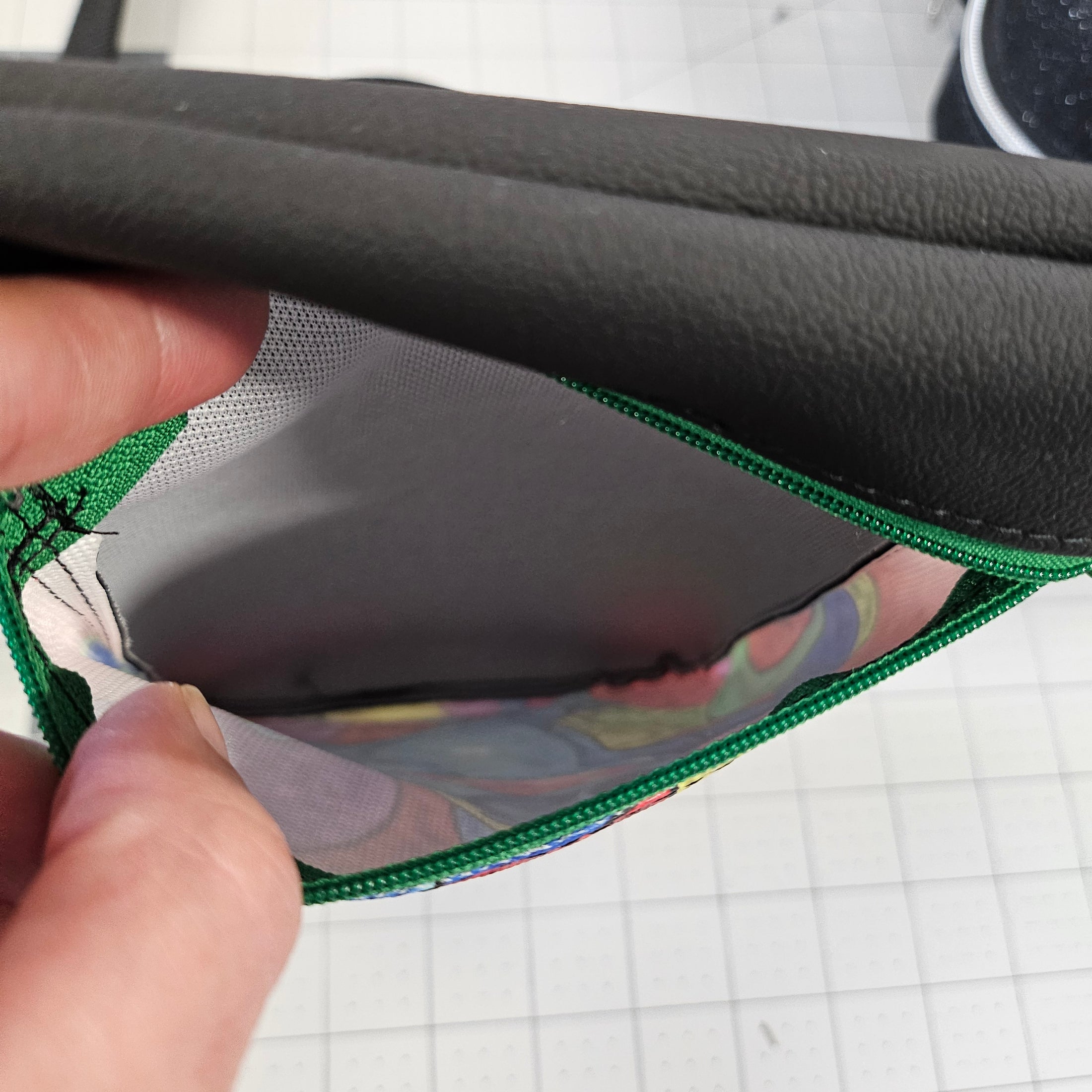Close-up of a hand holding a black and green bag with a colorful interior.