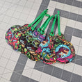 Load image into Gallery viewer, Dinosaur ornaments with green ribbon on a grid like surface.
