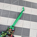 Load image into Gallery viewer, Green ribbon with a knot on a grid like surface.
