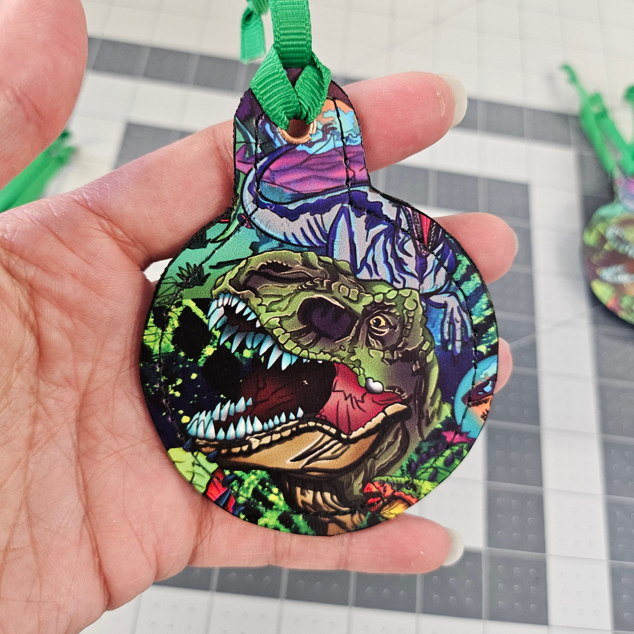 T Rex ornament with green ribbon held by a hand.