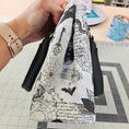 Load image into Gallery viewer, Hand holding a white clutch with black illustrations against a tiled wall background
