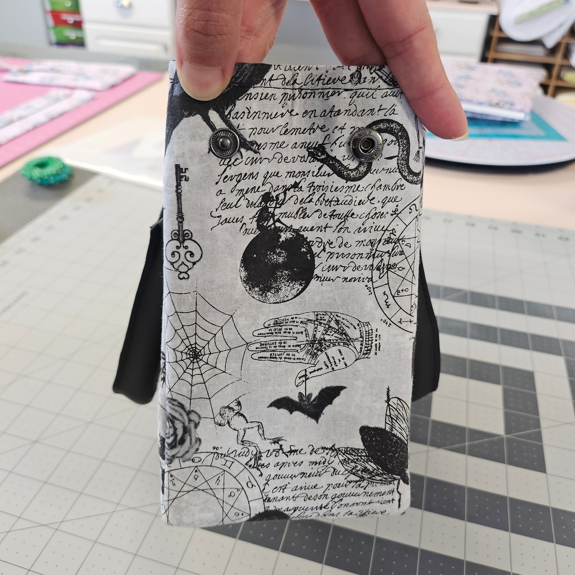 Hand holding a small rectangular pouch with black and white pattern on a grid background