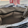 Load image into Gallery viewer, Close-up of a backpack zipper with a hand holding it open, against a blurred background.
