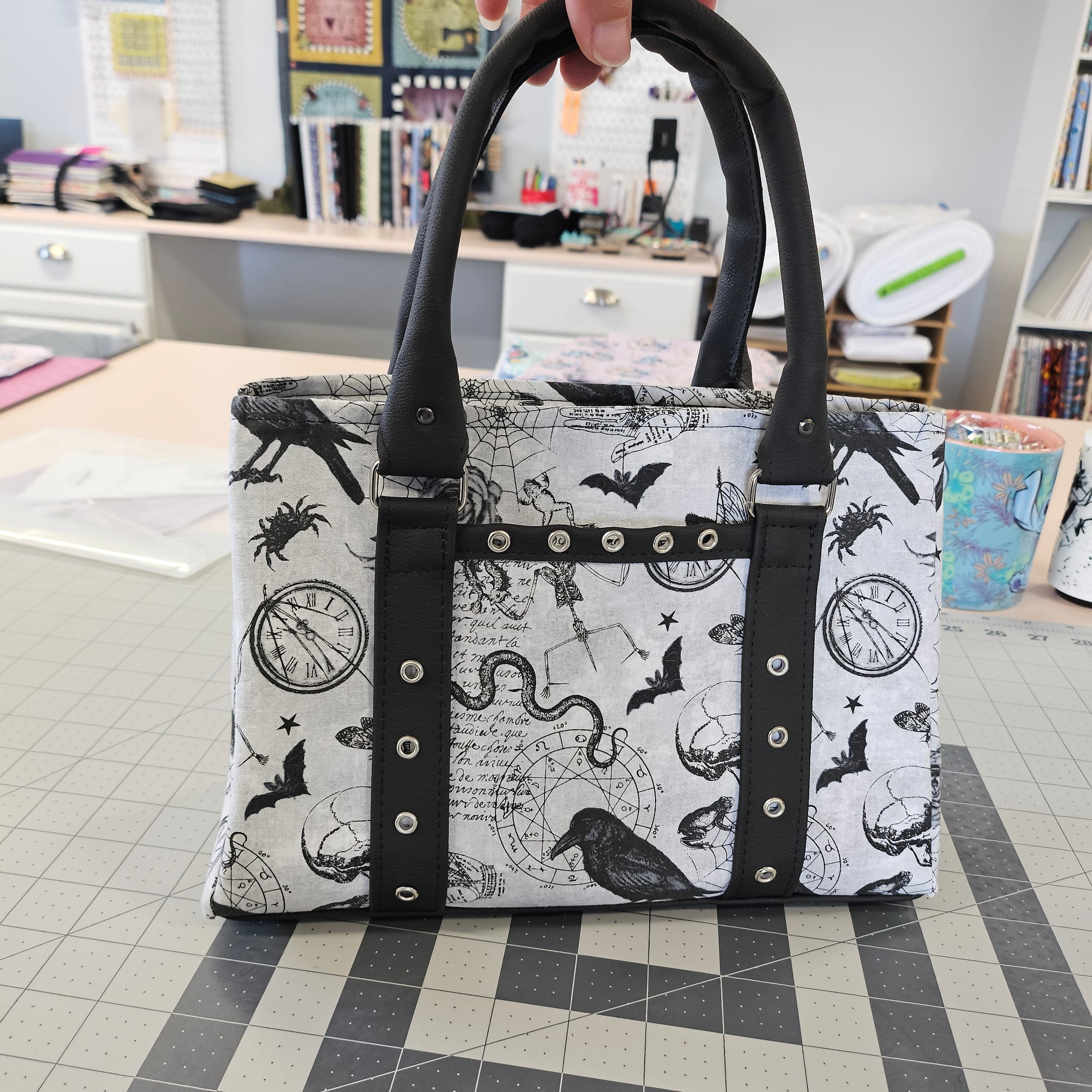 Handbag with black and white pattern held by a hand in a room with books and stationery.