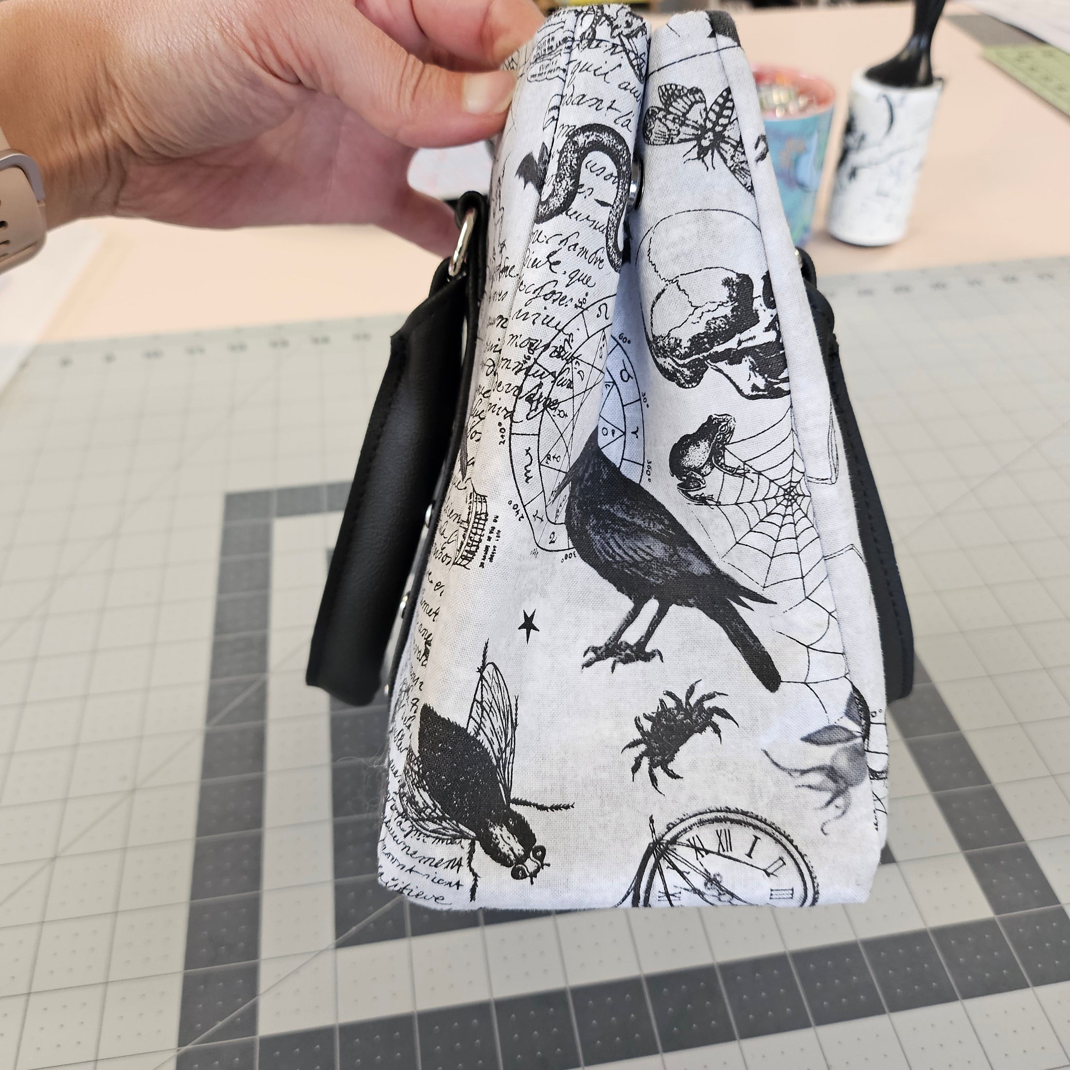 Hand holding a white clutch with black ink illustrations on a tiled floor background
