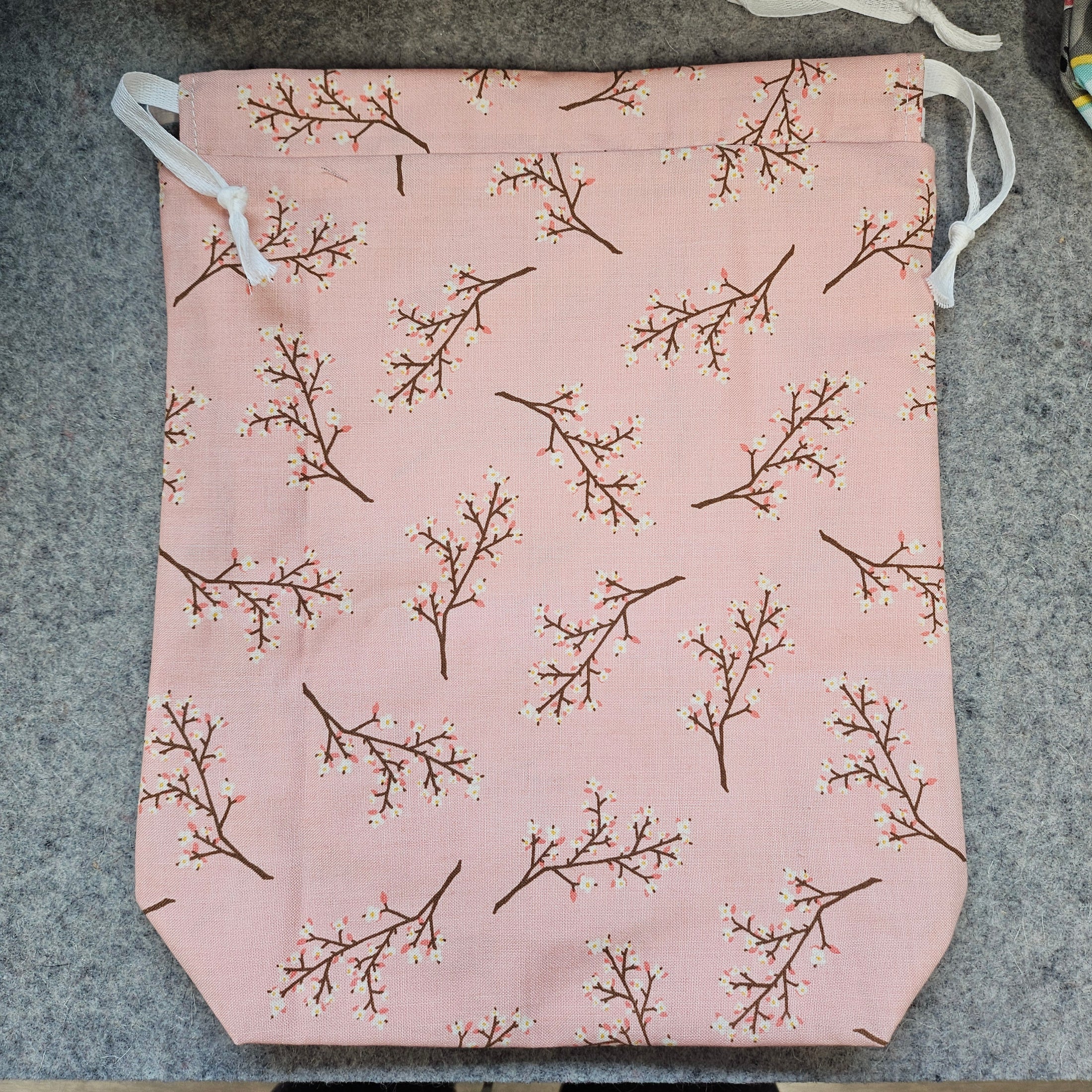 Pink drawstring bag with branch pattern on a gray surface