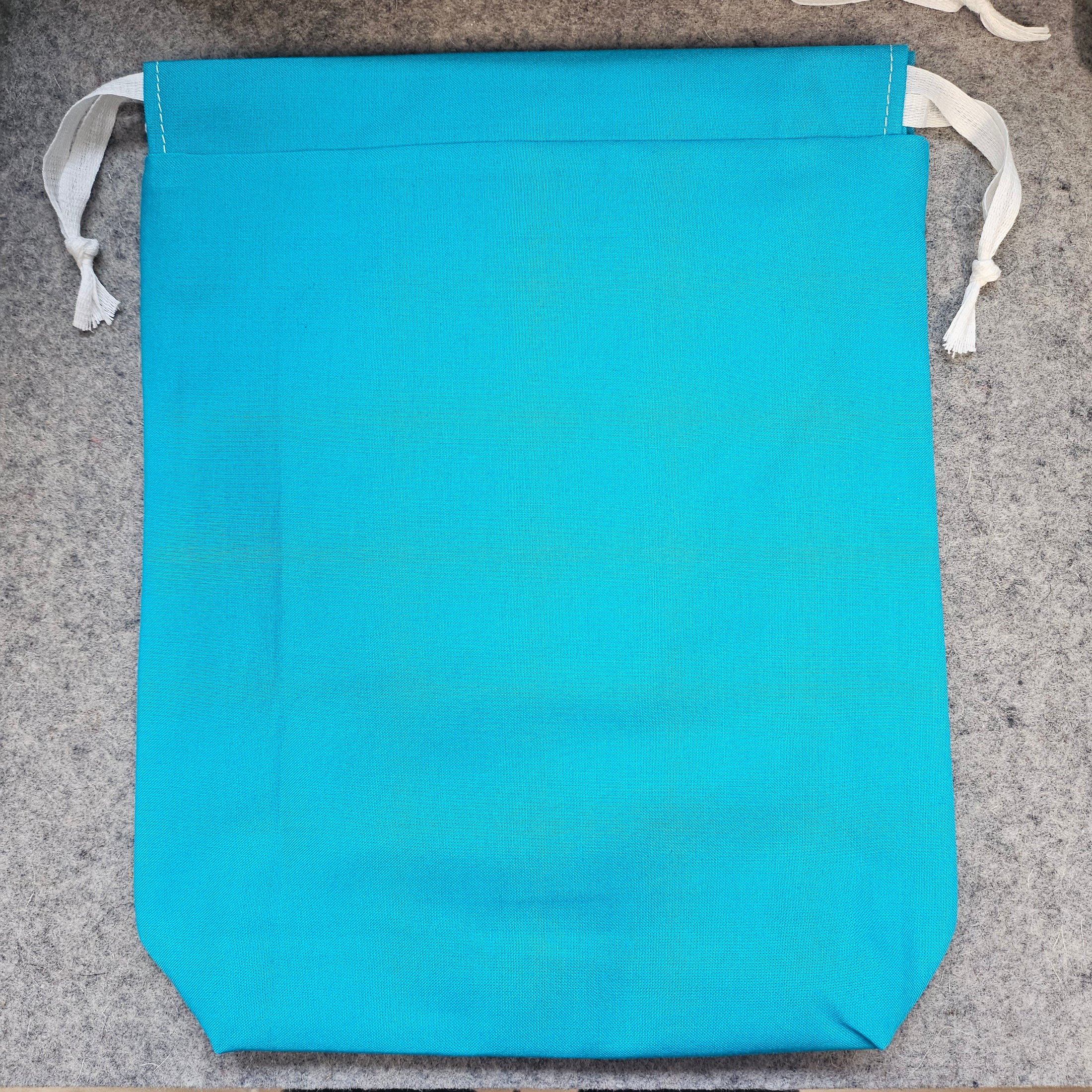 Blue fabric bag with white drawstrings on a gray surface