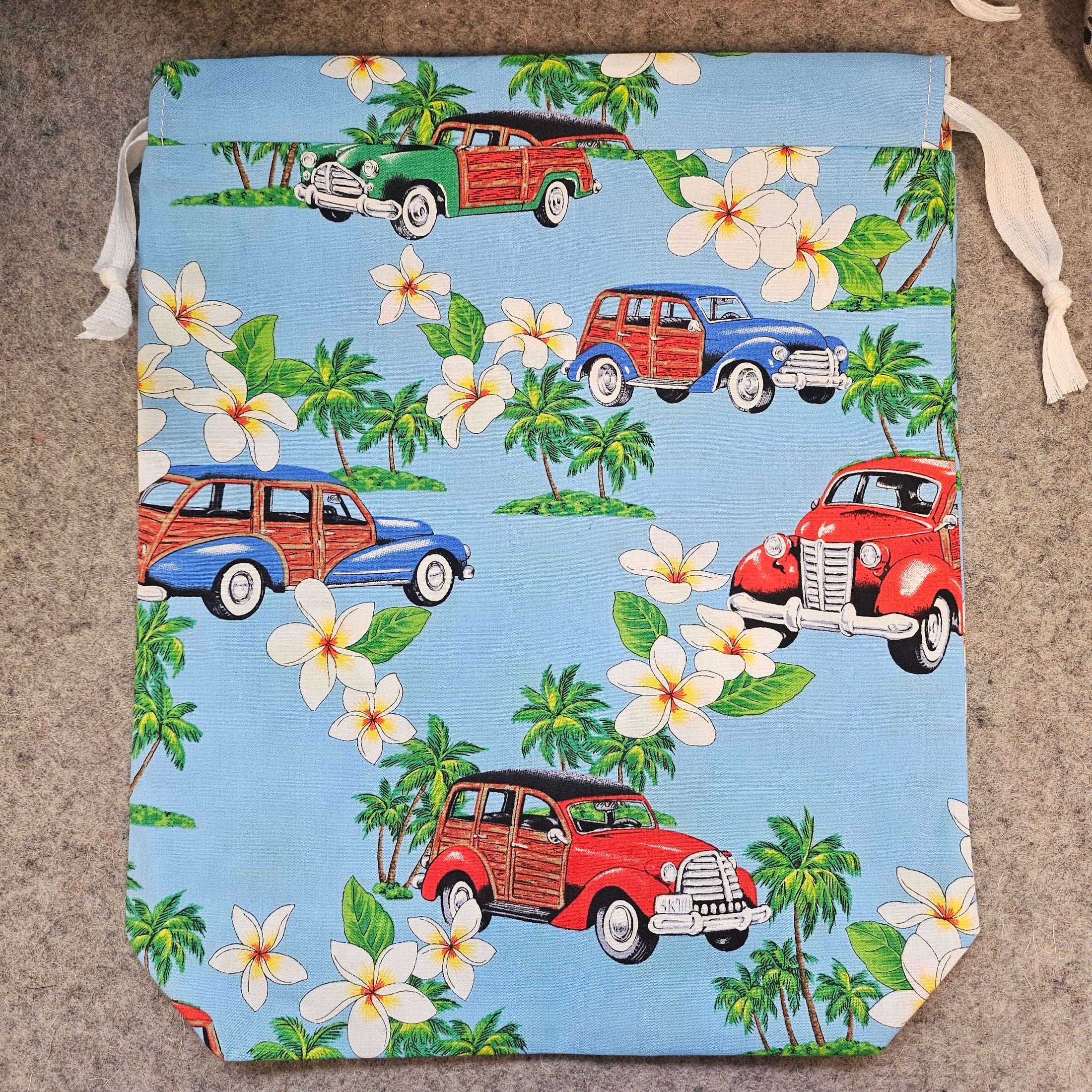 Light blue drawstring bag with white strings featuring palm trees and classic cars.