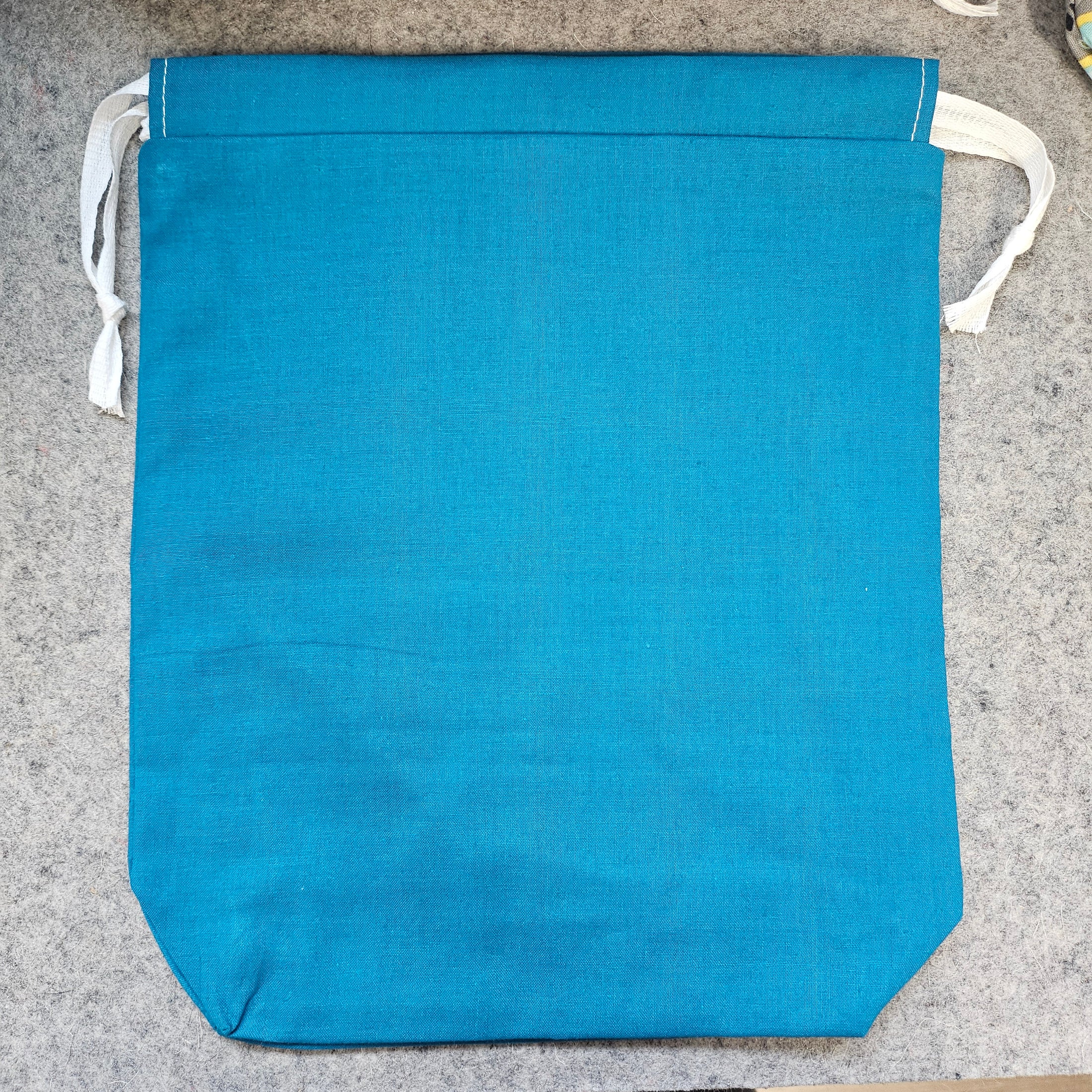 Dark turquoise drawstring bag with white string on a gray surface.