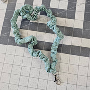 Turquoise skinny scrunchie lanyard laying on a gray cutting mat. 