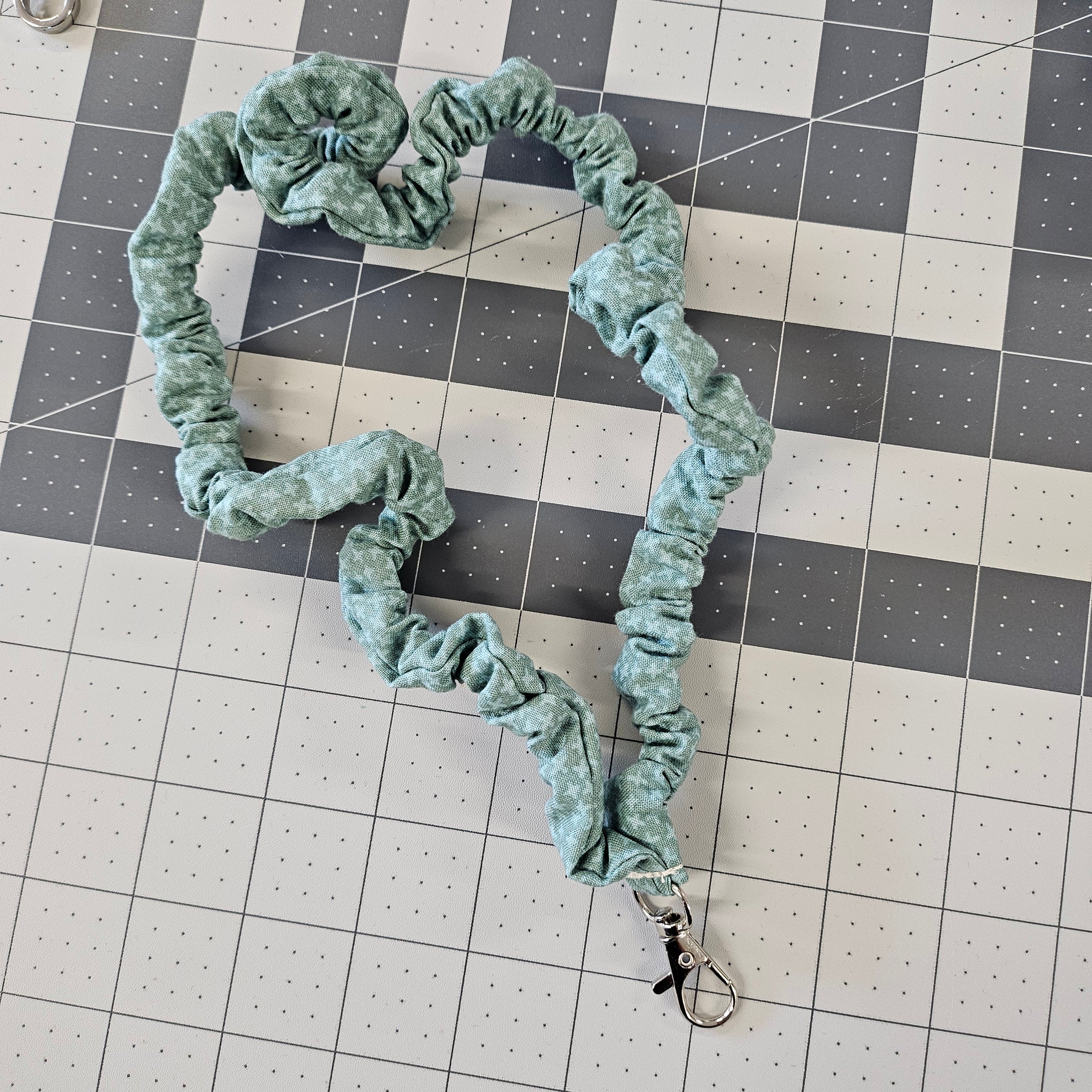 Turquoise skinny scrunchie lanyard laying on a gray cutting mat. 