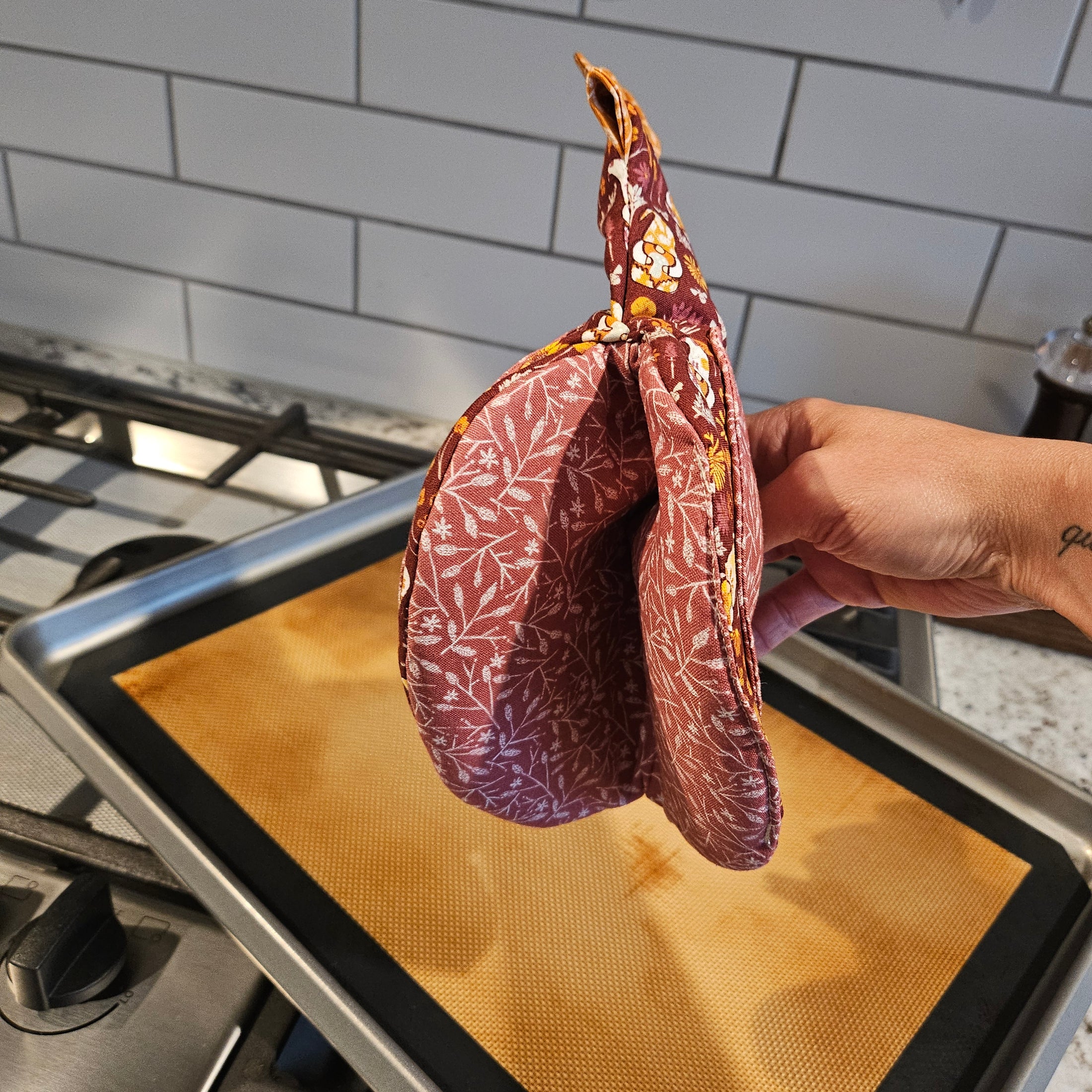 Hand holding a floral-patterned pot lid over an open grill.