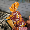 Load image into Gallery viewer, Floral-patterned fabric with orange accents held over a tiled floor
