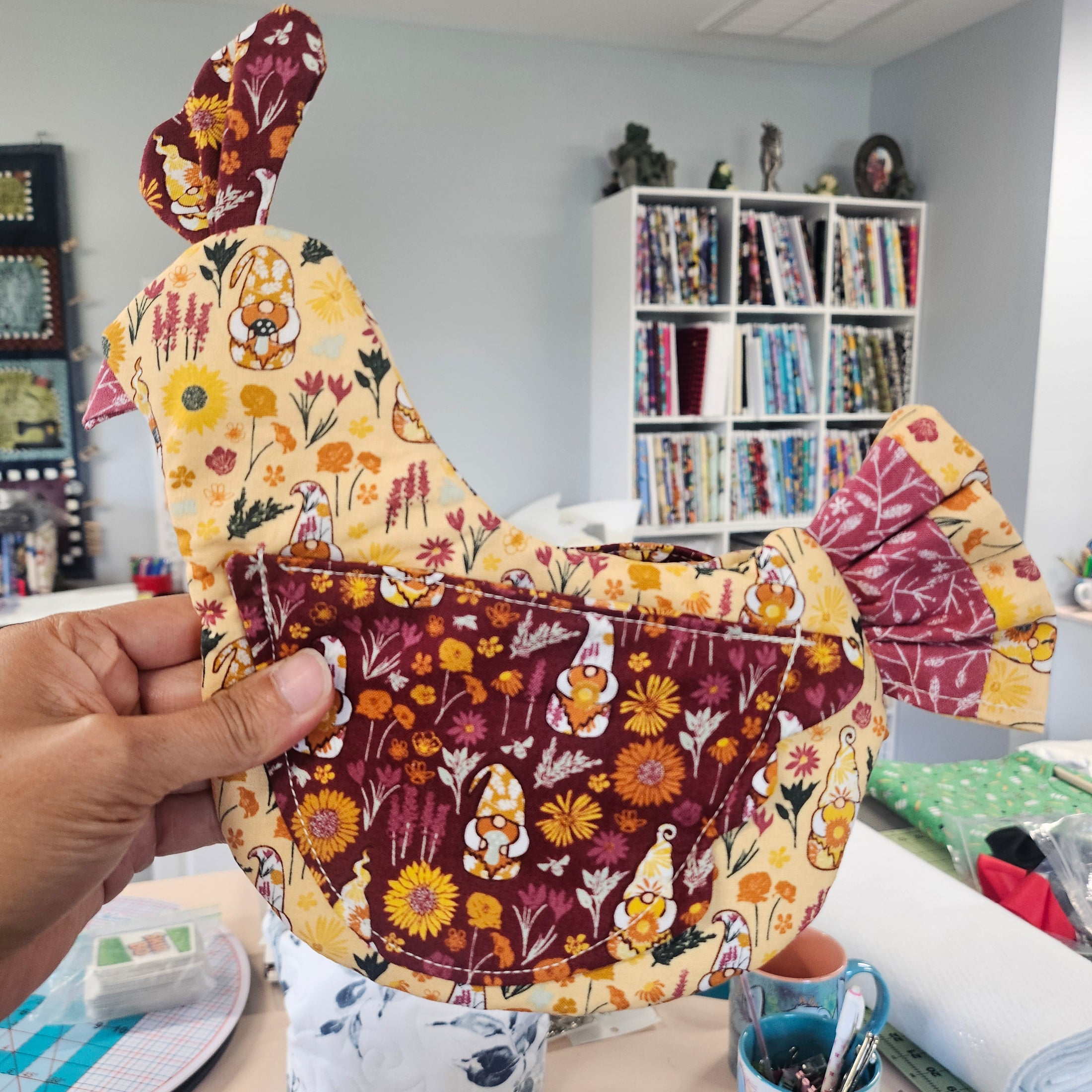 Handmade fabric chicken with floral patterns held in front of a fabric shelf.