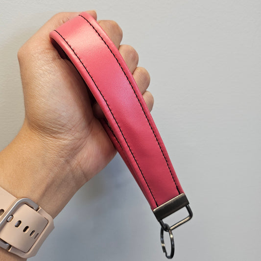 Pink leather strap with a metal buckle held in a hand against a neutral background