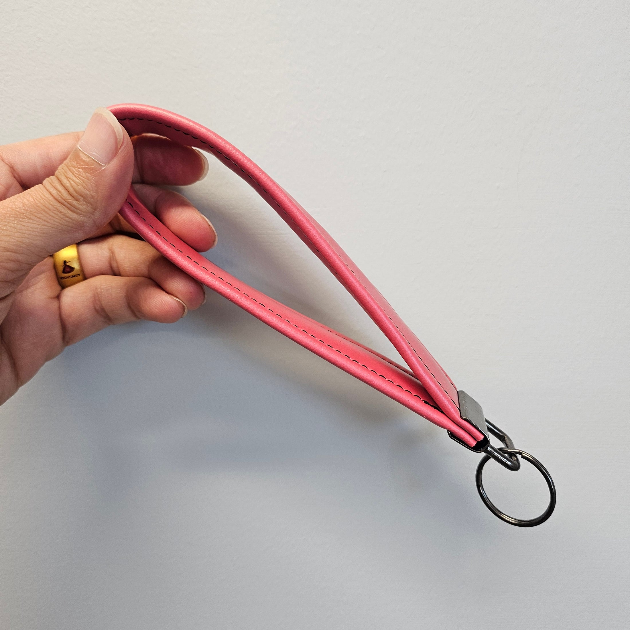 Hand holding a pink leather strap with a metal ring against a light gray background