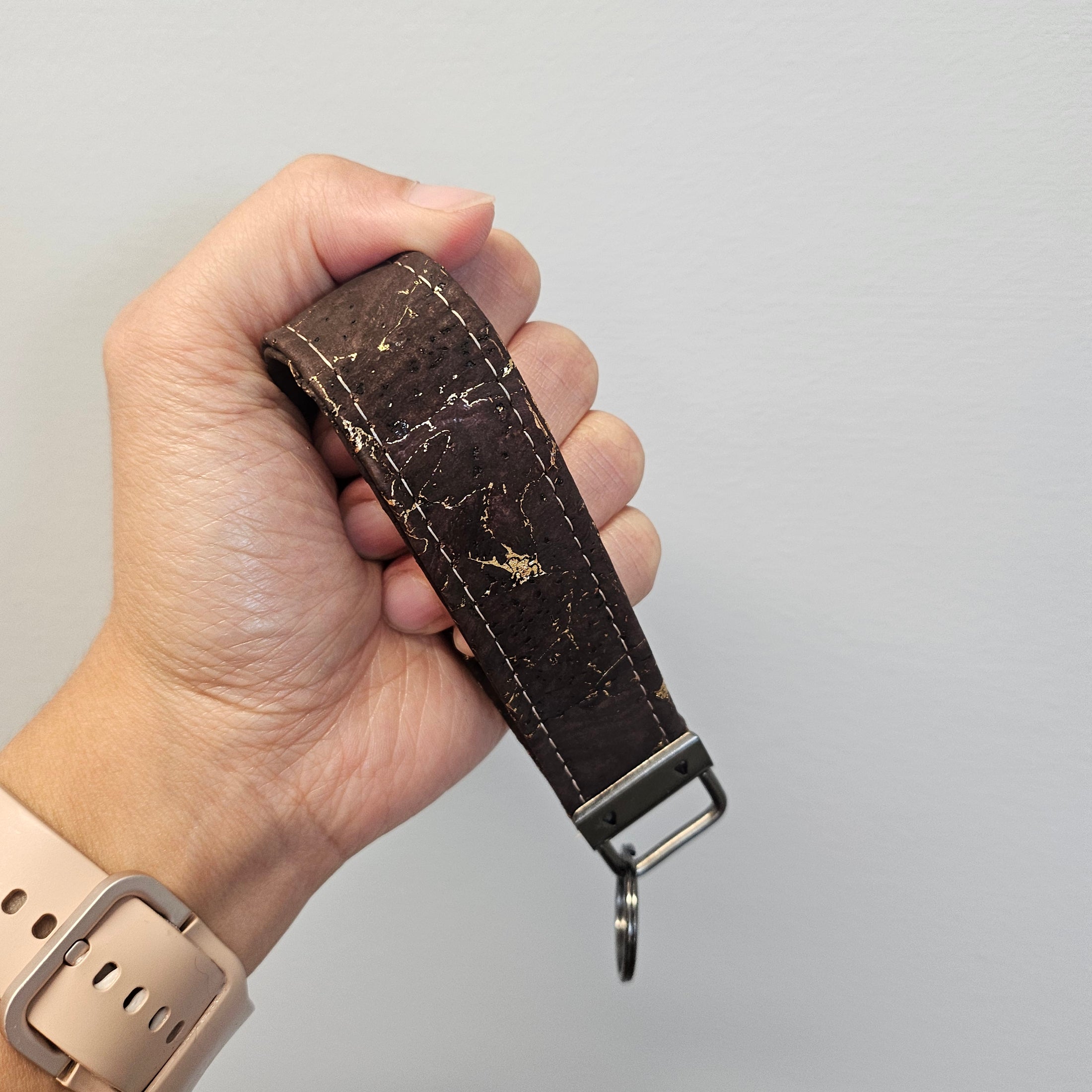 Gold and brown key strap wristlet held by a hand against a light gray backdrop.