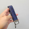 Load image into Gallery viewer, Blue and black cork key chain being held by a hand against a light gray background.
