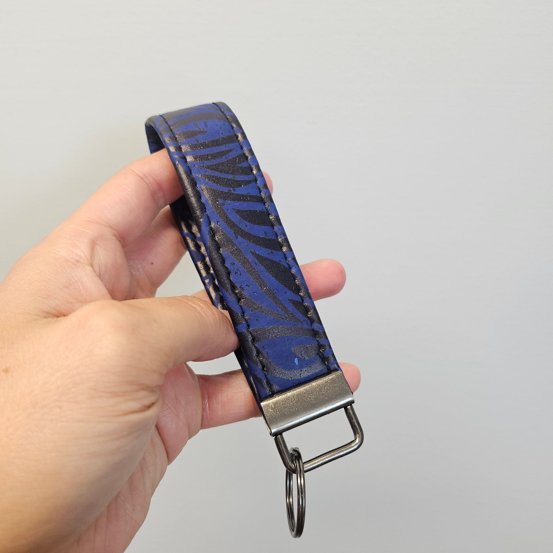 Blue and black cork key chain being held by a hand against a light gray background.